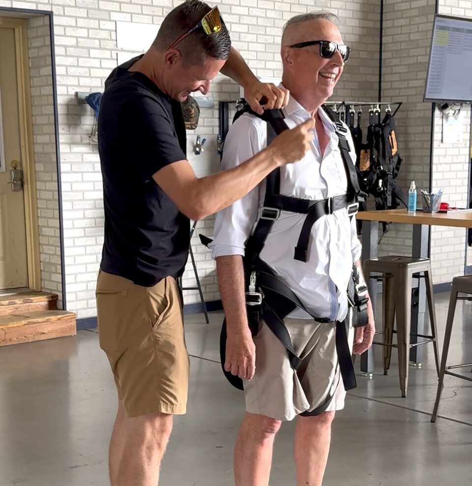 a participant in the spectator experience tries on the tandem skydiving harness